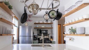 Una cocina moderna con electrodomésticos de acero inoxidable, estantes de madera y utensilios colgados.