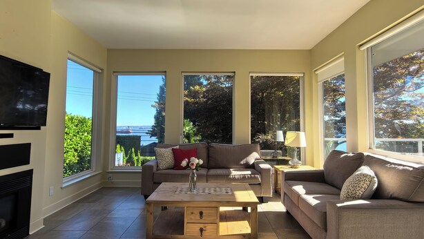 A spacious living room with a fireplace, large windows, and a television.