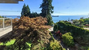 A balcony with a view of the sea, trees, and a distant cityscape.