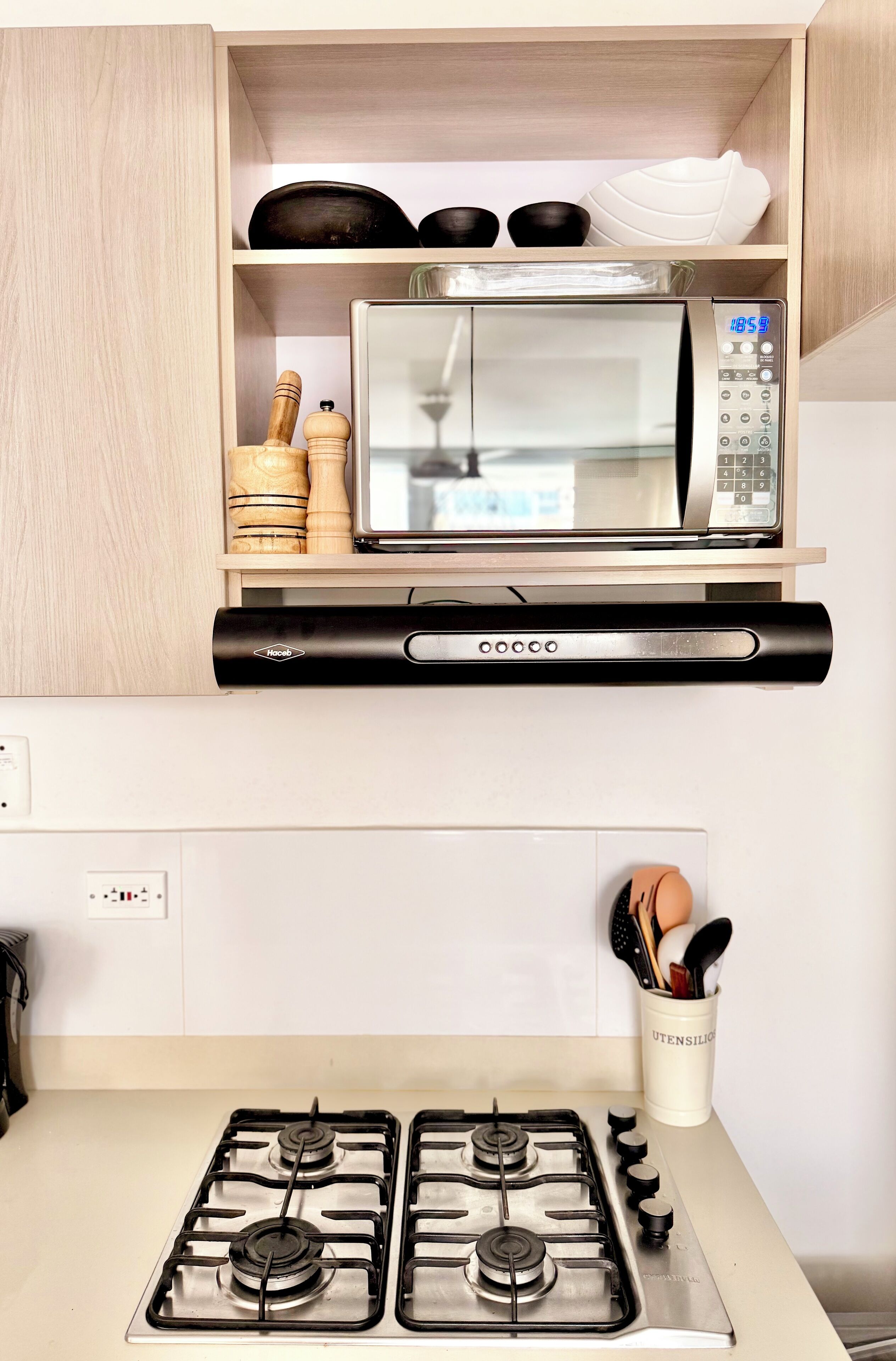 Une cuisine avec un four à micro-ondes posé sur une étagère en bois, une cuisinière à quatre brûleurs et un porte-ustensiles.