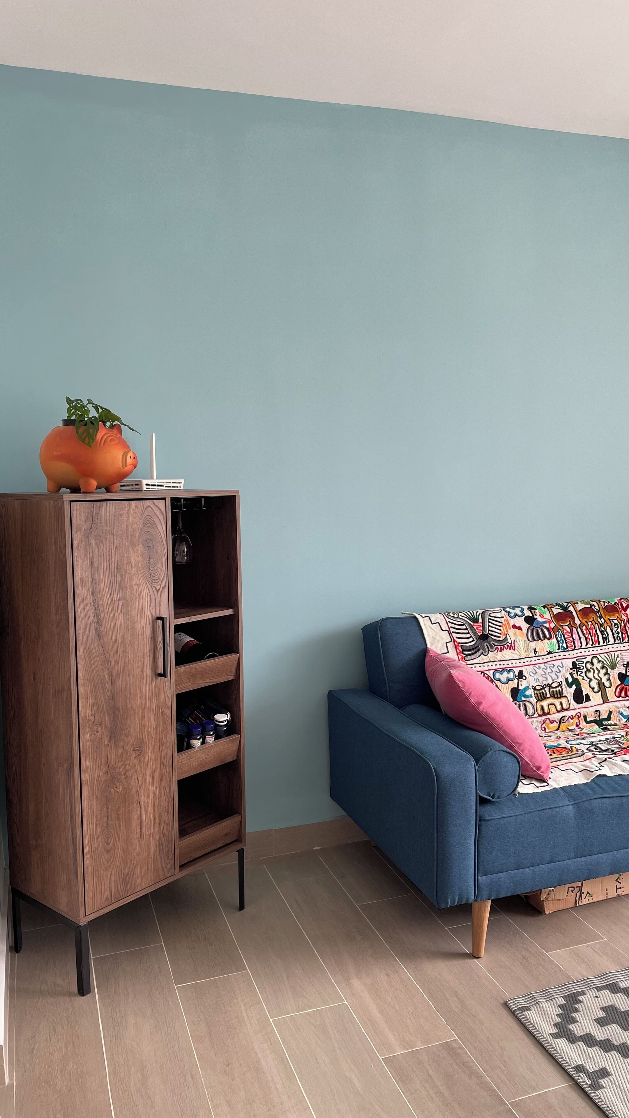 Een woonkamer met een blauwe bank, een houten kast en een kleurrijk plaid.