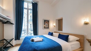 A hotel room with a large bed, a window with curtains, a radiator, a wall-mounted light fixture, and a framed picture. - Parisian Charm by the Louvres (Paris)