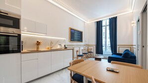 A modern kitchen with white cabinets, a wooden dining table, and a blue sofa in the living area. - Parisian Charm by the Louvres (Paris)