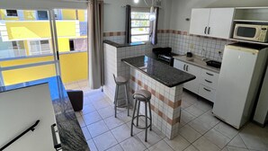 A compact kitchen with a central island, white cabinets, a microwave, and a refrigerator. - Pousada Village (Florianopolis)