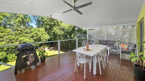 Um pátio externo com mesa de jantar, cadeiras, churrasqueira e ventilador de teto.