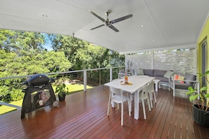 Een terras buiten met een eettafel, stoelen, een barbecue en een plafondventilator.