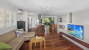 Uma sala de estar moderna com piso de madeira, um sofá bege, uma mesa redonda pequena e uma TV de tela plana na parede.