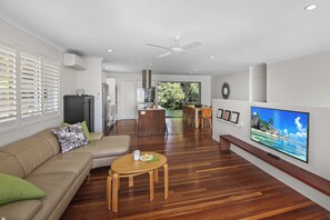 Een moderne woonkamer met een houten vloer, een beige bank, een klein rond tafeltje en een flatscreen televisie die aan de muur is bevestigd.