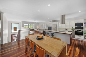 Una cocina moderna con una mesa de comedor de madera, armarios blancos y electrodomésticos de acero inoxidable.