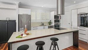 Cozinha moderna com ilha central, banquetas, geladeira de aço inoxidável e forno embutido.