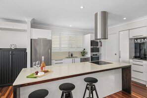 Een moderne keuken met een centraal eiland, barkrukken, een roestvrijstalen koelkast en een inbouwoven.
