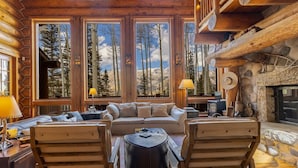 A log cabin interior with a fireplace, large windows, and a cozy seating area. - Ute Lodge | Hot Tub, Walk to Trails, Big Views! (Mountain Village)