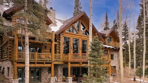 A log cabin with multiple balconies, stone foundations, and a snowy landscape. - Ute Lodge | Hot Tub, Walk to Trails, Big Views! (Mountain Village)