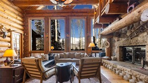 A log cabin interior with a fireplace, large windows, and a cozy seating area. - Ute Lodge | Hot Tub, Walk to Trails, Big Views! (Mountain Village)