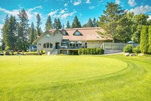A golf course with a clubhouse featuring a large windowed entrance, outdoor seating, and a well-maintained lawn.
