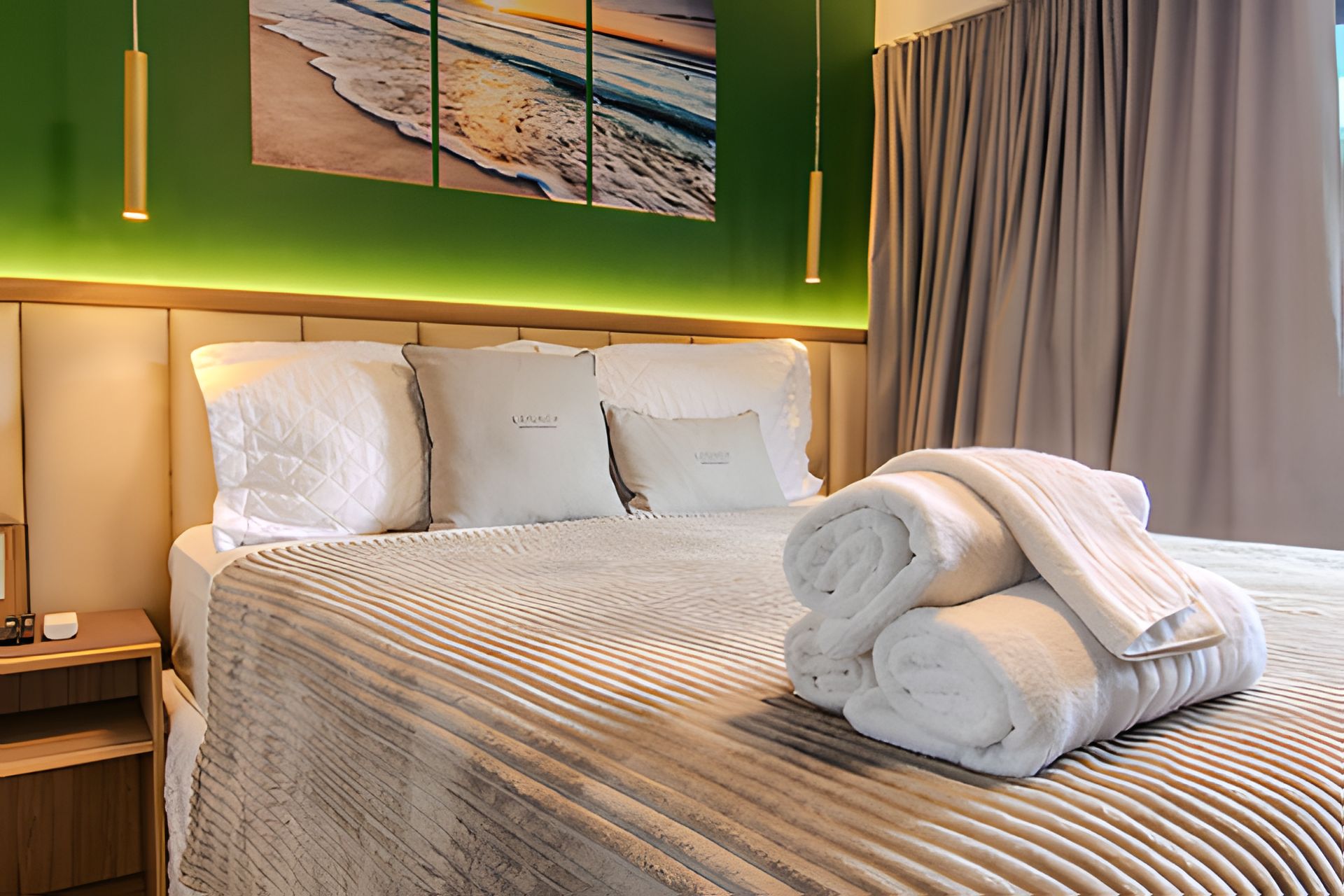 Una cama bien hecha con una colcha a rayas, una toalla doblada y un cuadro con una playa en la pared.