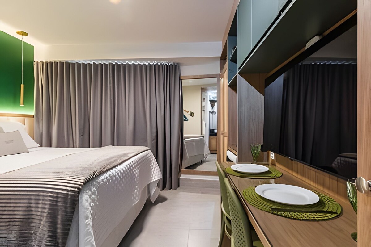 A hotel room with a bed, a bathroom with a mirror, and a dining area with a table and chairs.