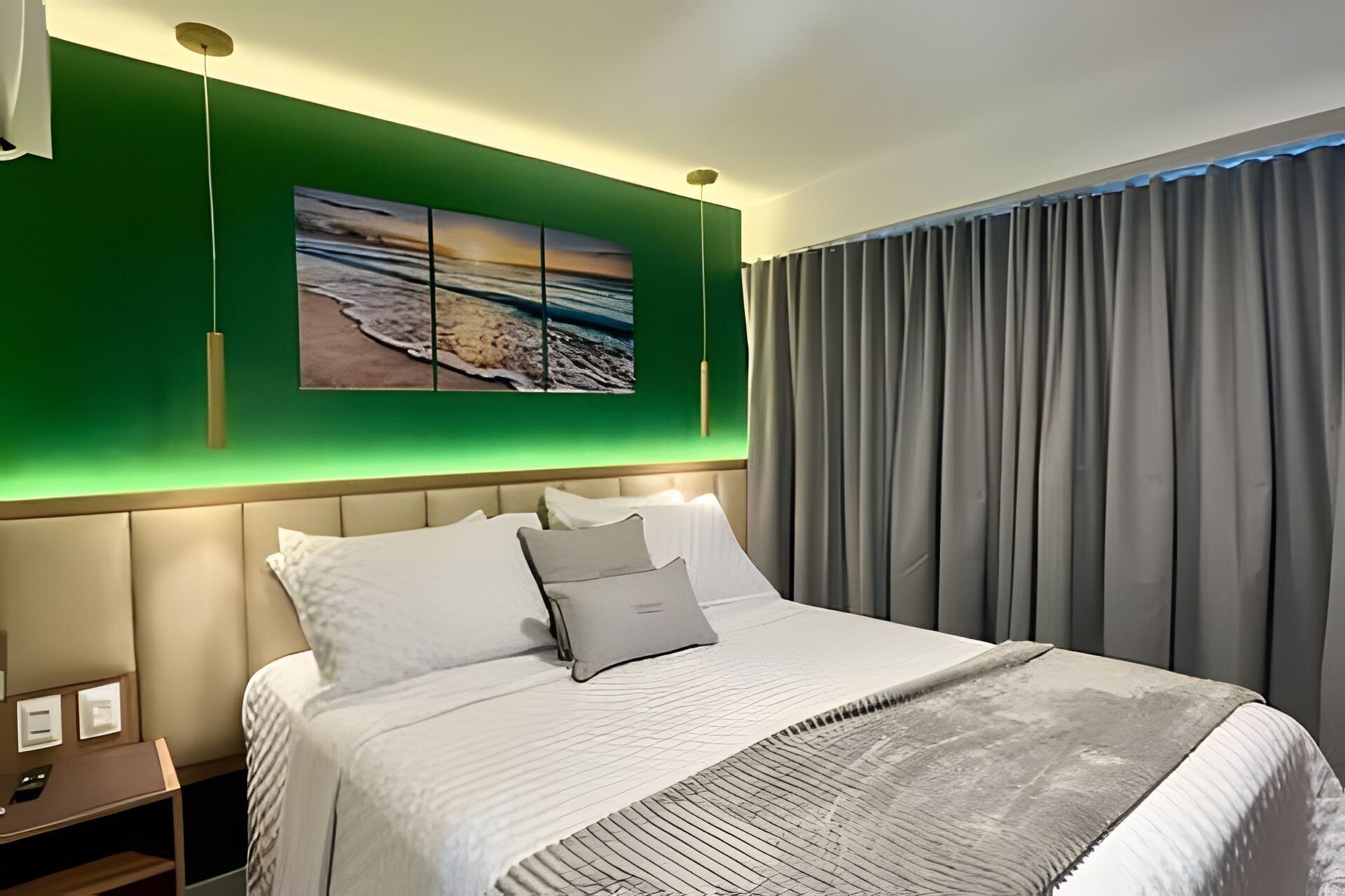 Une chambre d’hôtel avec un lit, une table de chevet, une œuvre d’art accrochée au mur et une fenêtre avec des rideaux.