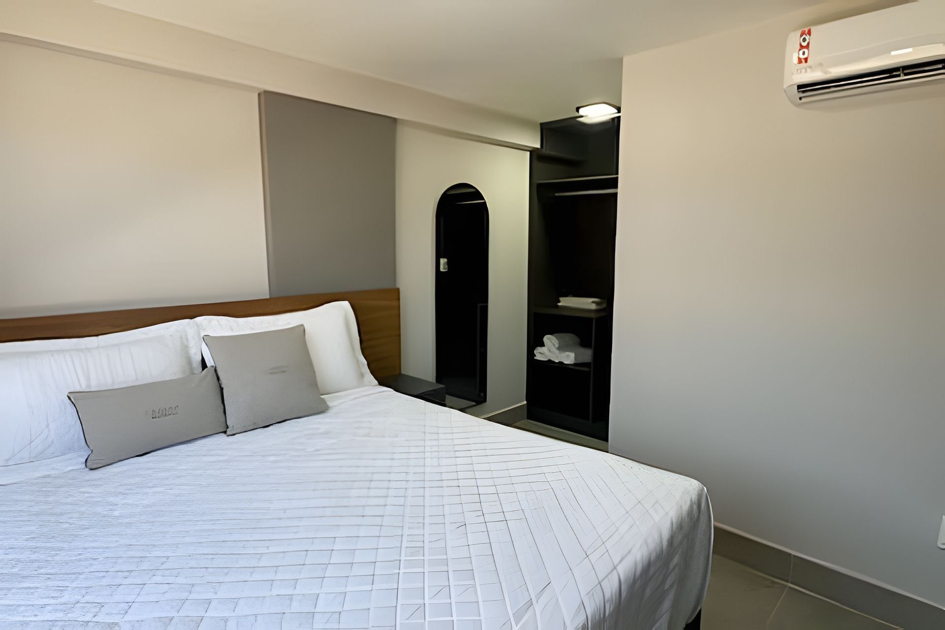 A hotel room with a bed, a wardrobe, and an air conditioning unit.