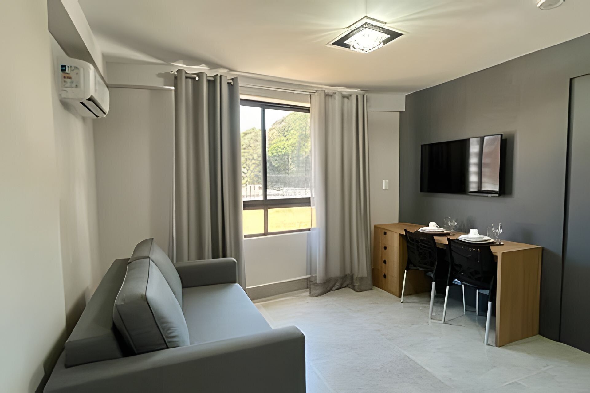 Une chambre moderne équipée d’un canapé, d’un bureau avec des chaises, d’un téléviseur à écran plat et d’une fenêtre avec des rideaux.