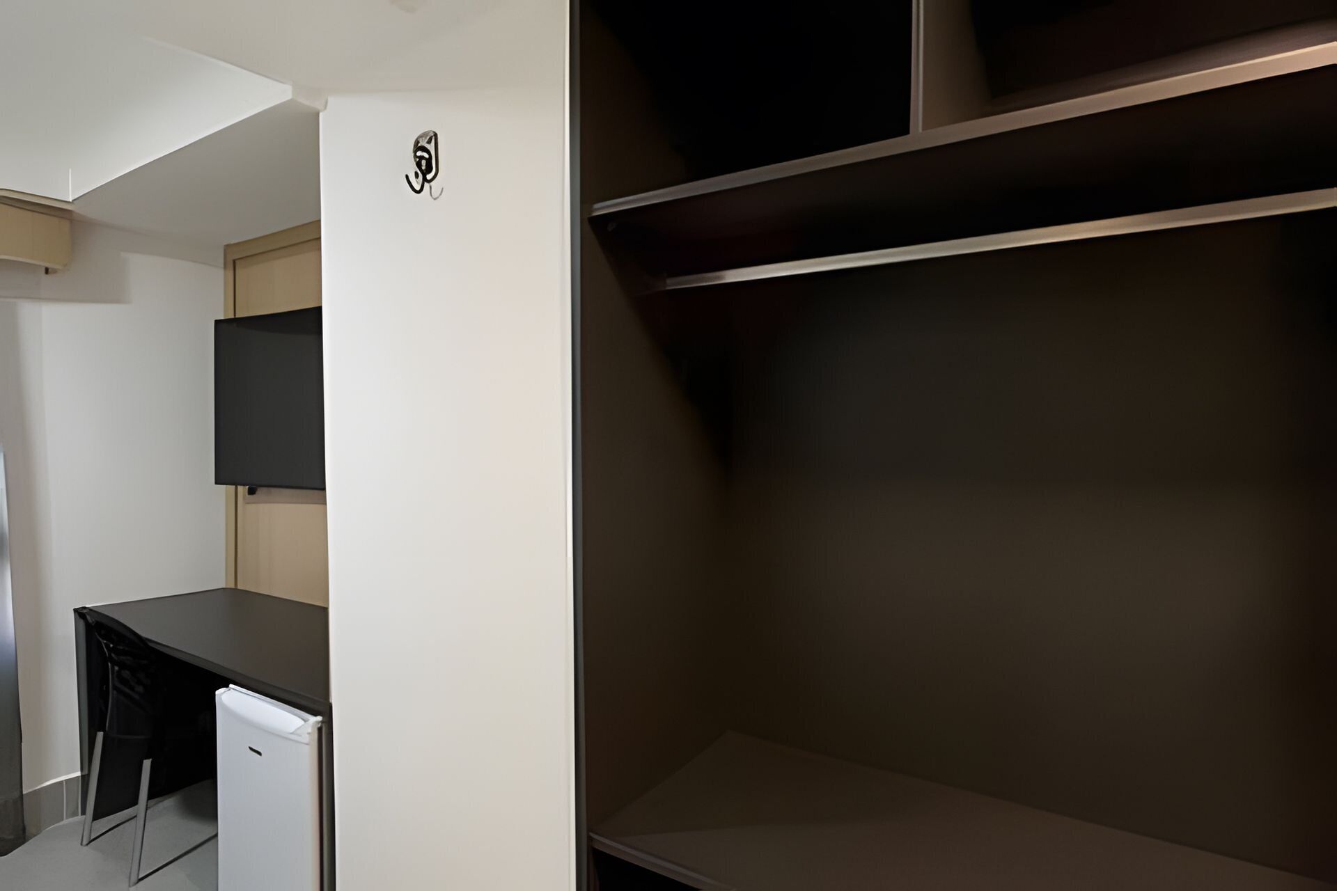 Una habitación con escritorio, refrigerador pequeño, televisor montado en la pared y estanterías integradas.