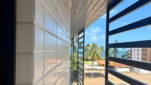 A balcony with a view of a beach, palm trees, and buildings. - Legacy Suites (João Pessoa)