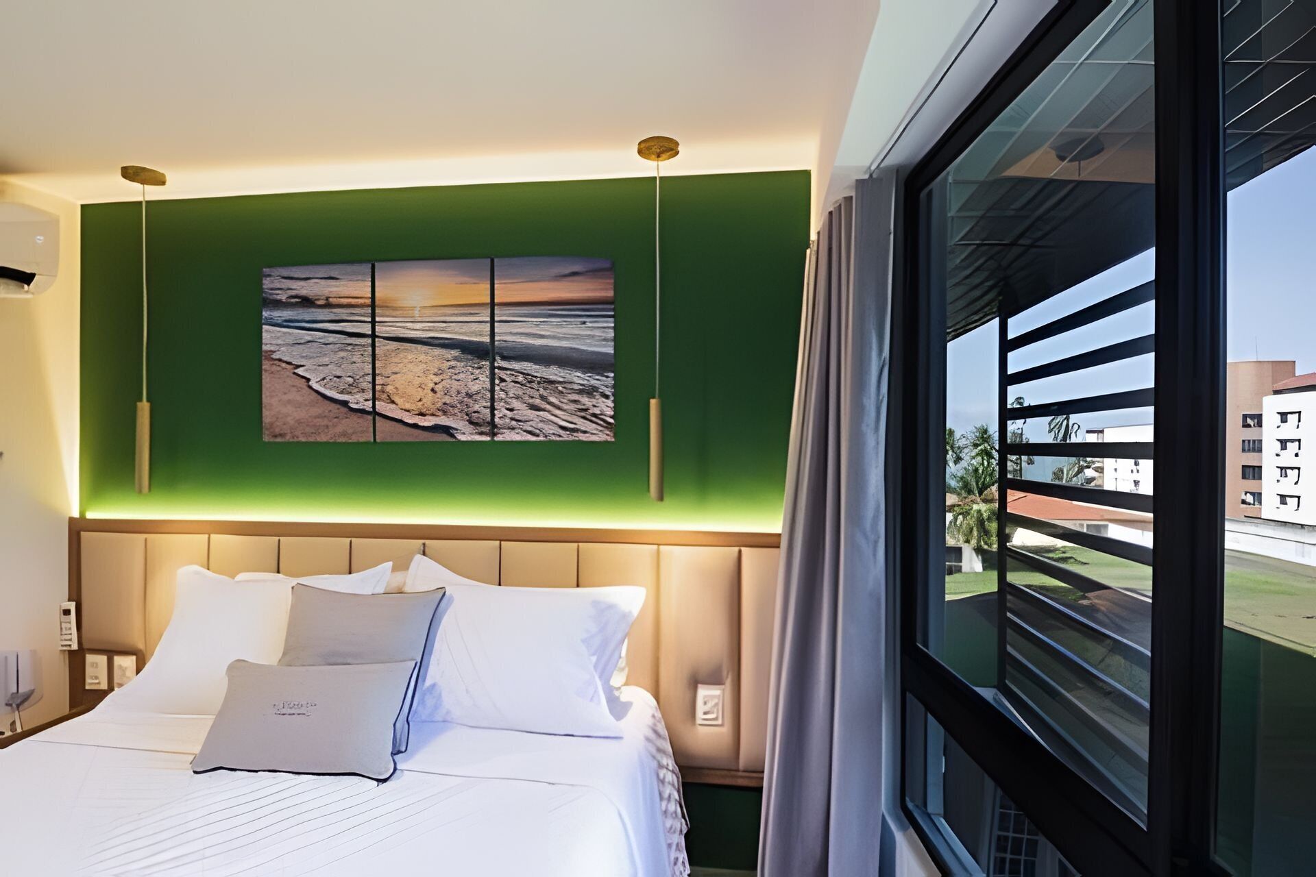 Habitación de hotel con cama, pared verde, ventana grande y una pintura de una playa.