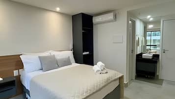 Habitación de hotel con cama, armario, aire acondicionado, baño con lavamanos y espejo.