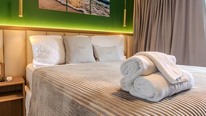 A neatly made bed with a striped bedspread, a folded towel, and a painting of a beach scene on the wall. - Legacy Suites (João Pessoa)