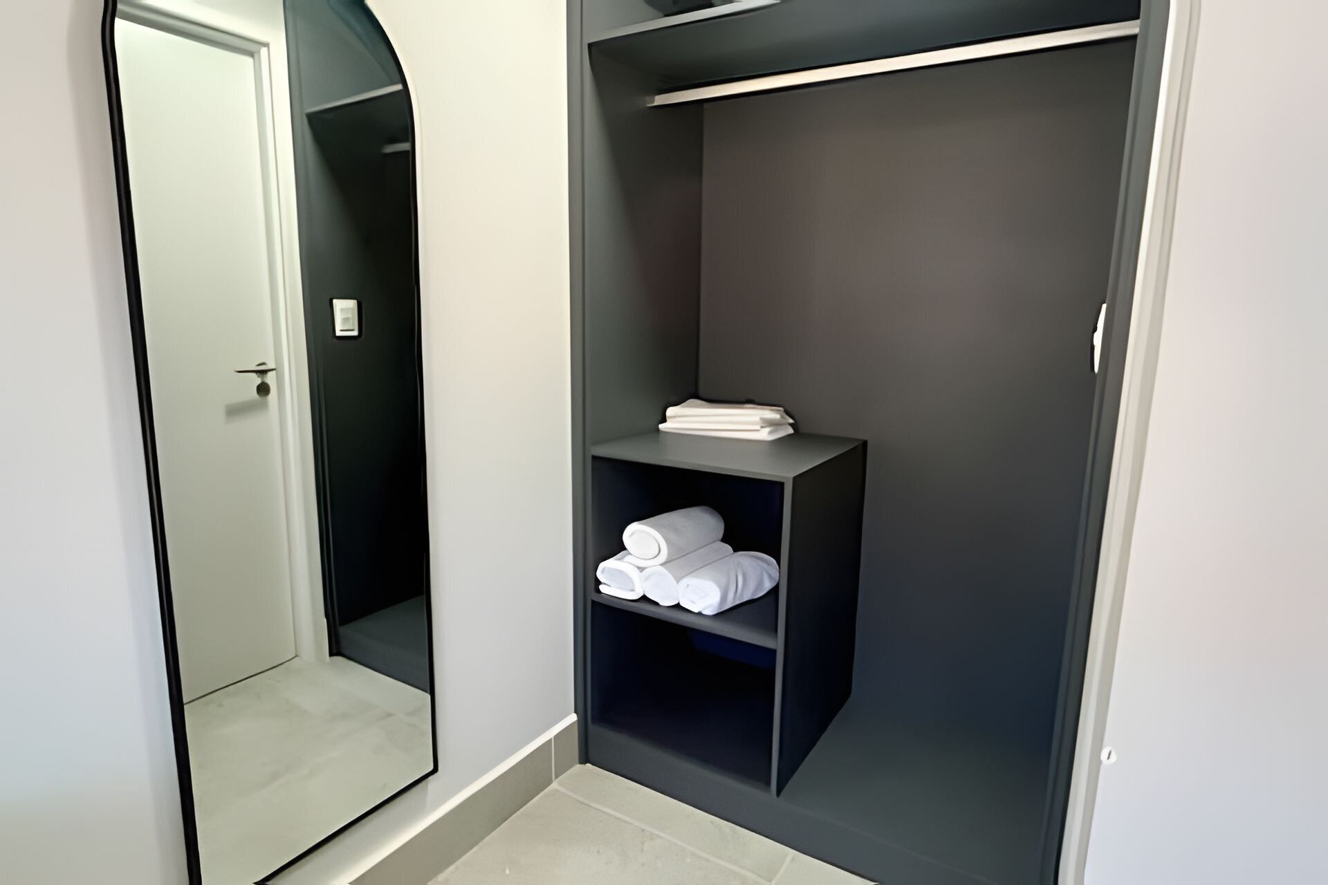 Een inloopkast met een spiegeldeur, een plank met opgevouwen handdoeken, en een donkerhouten garderobe.