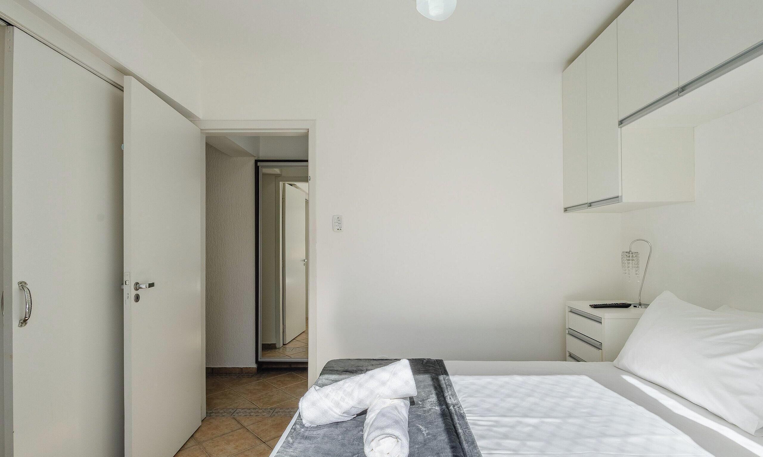 Een hotelkamer met een bed, nachtkastje met lamp, kledingkast en een zichtbare badkamer door een open deur.
