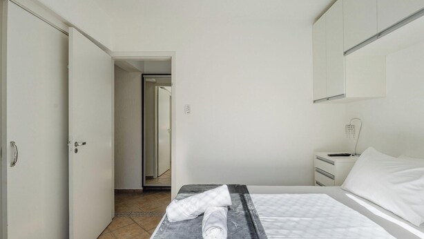 A hotel room with a bed, a bedside table with a lamp, a wardrobe, and a bathroom visible through an open door. - Apartment in a Seaside Building - Iptr0082 (Balneário Camboriú)