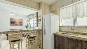 A kitchen with a refrigerator, a sink, and a dining area with chairs. - Apartment in a Seaside Building - Iptr0082 (Balneário Camboriú)