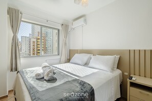 Une chambre d’hôtel comprenant un lit, une fenêtre avec des rideaux, un appareil de climatisation et une table de chevet avec une télécommande.