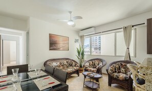 Un salon avec des meubles en osier, un ventilateur de plafond et une grande fenêtre avec des rideaux.