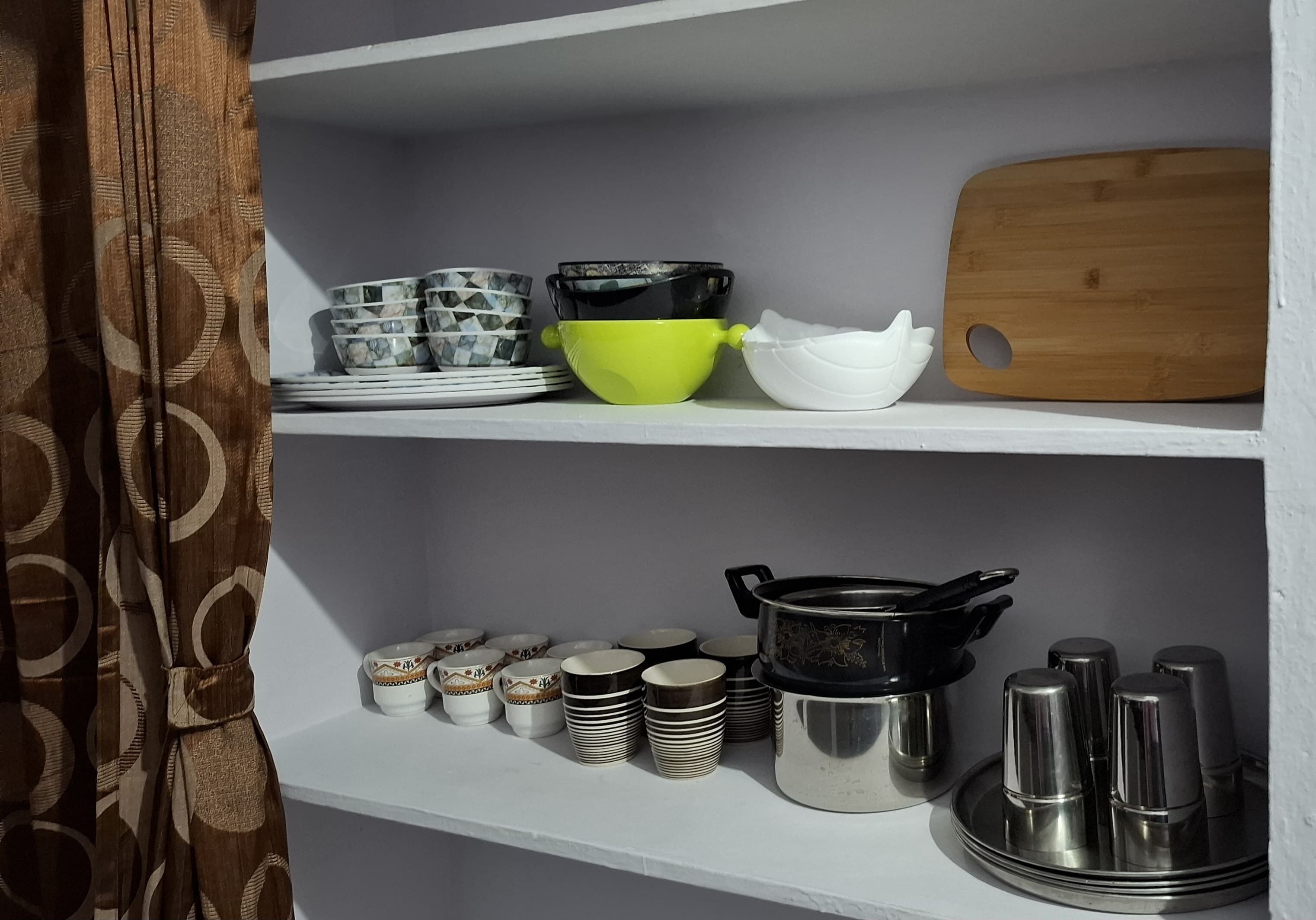 A kitchen shelf with various dishes and utensils, including bowls, plates, and a cutting board.