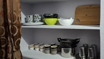 A kitchen shelf with various dishes and utensils, including bowls, plates, and a cutting board.