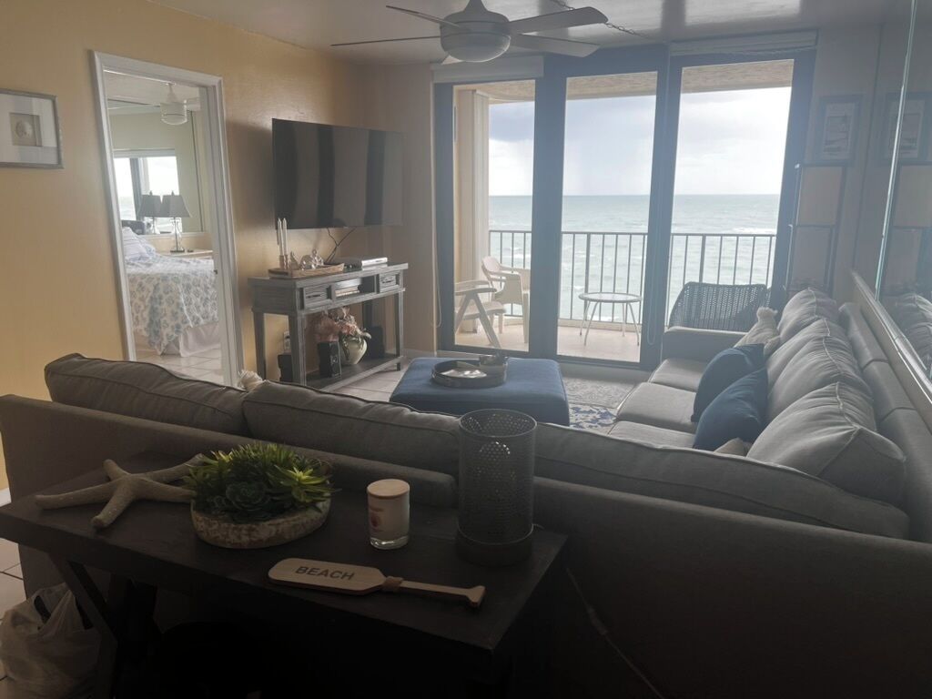 Un salon avec un canapé, une table basse et un téléviseur. Il y a un balcon avec vue sur l’océan.