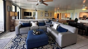 A modern living room with a grey sectional sofa, a blue ottoman, and a patterned rug.