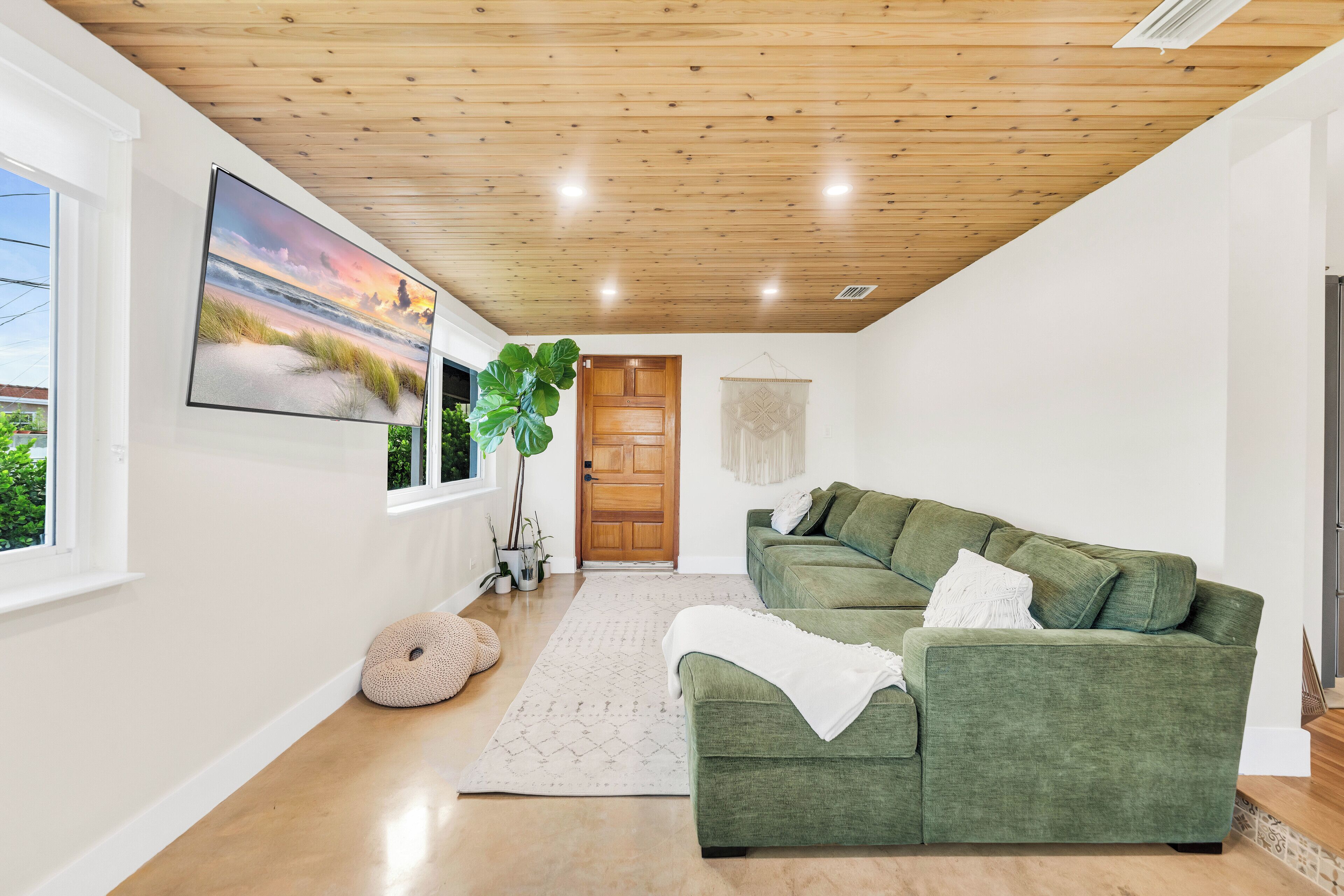 Een moderne woonkamer met een groene bank, een groot schilderij en een houten plafond.
