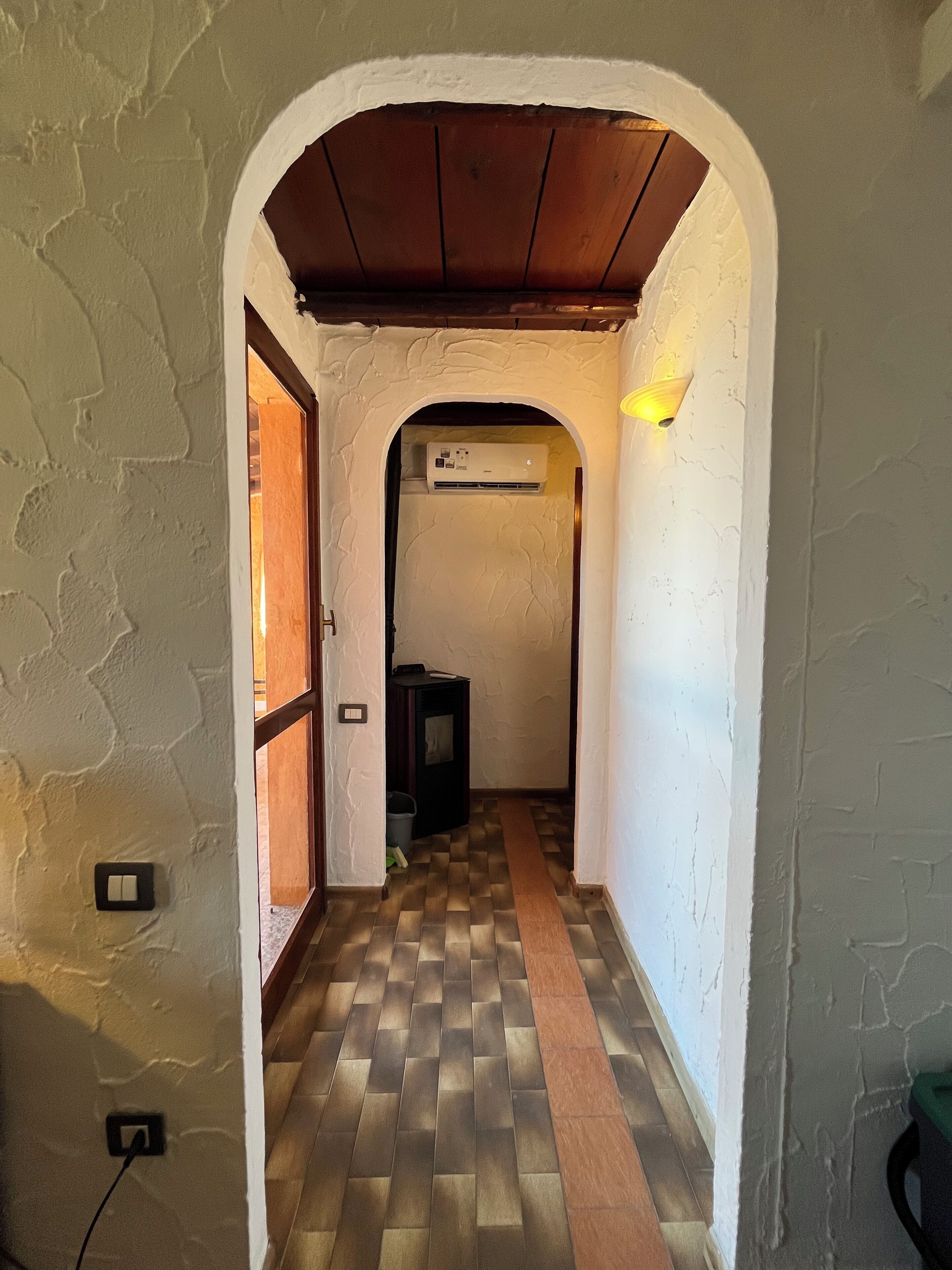Un couloir voûté avec un revêtement de sol à motifs, un climatiseur fixé au mur et un luminaire.