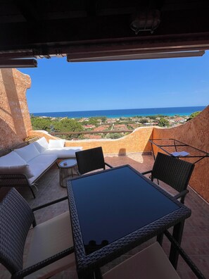 Um pátio externo com mesa e cadeiras, um sofá e vista para o mar e a cidade.