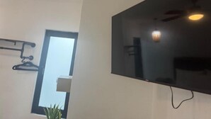A modern room with a large flat-screen TV mounted on the wall, a window with a view, and a ceiling fan.