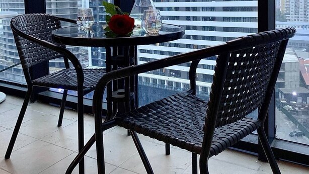 A balcony with two wicker chairs and a glass table, featuring a rose and a glass of water. - Enjoyable apartment with AC in charming Batumi (Batumi)