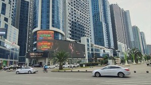 A modern urban street with high-rise buildings, a prominent curved skyscraper, and a billboard advertising a hotel. - Enjoyable apartment with AC in charming Batumi (Batumi)