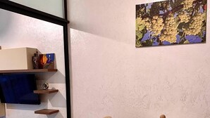 A dining area with a round table, two chairs, a wooden cabinet, and a wall-mounted shelf with decorative items. - Enjoyable apartment with AC in charming Batumi (Batumi)