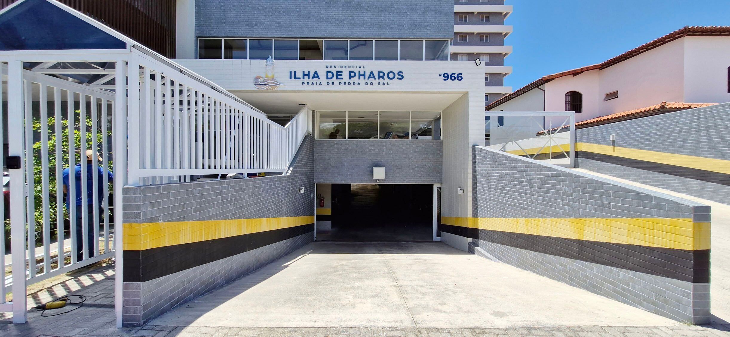 A residential building entrance with a gated driveway, a staircase, and a clear sky.