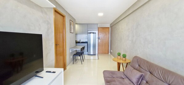 A modern living room with a flat-screen TV, a sofa, and a small round table with two potted plants.
