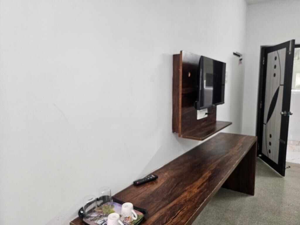 A room with a wooden bench, a mounted TV, and a door with a black frame.