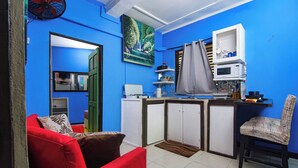 A compact living space with a kitchenette, a red sofa, a patterned armchair, and a blue wall. - Tropic Nook (Gros Islet)